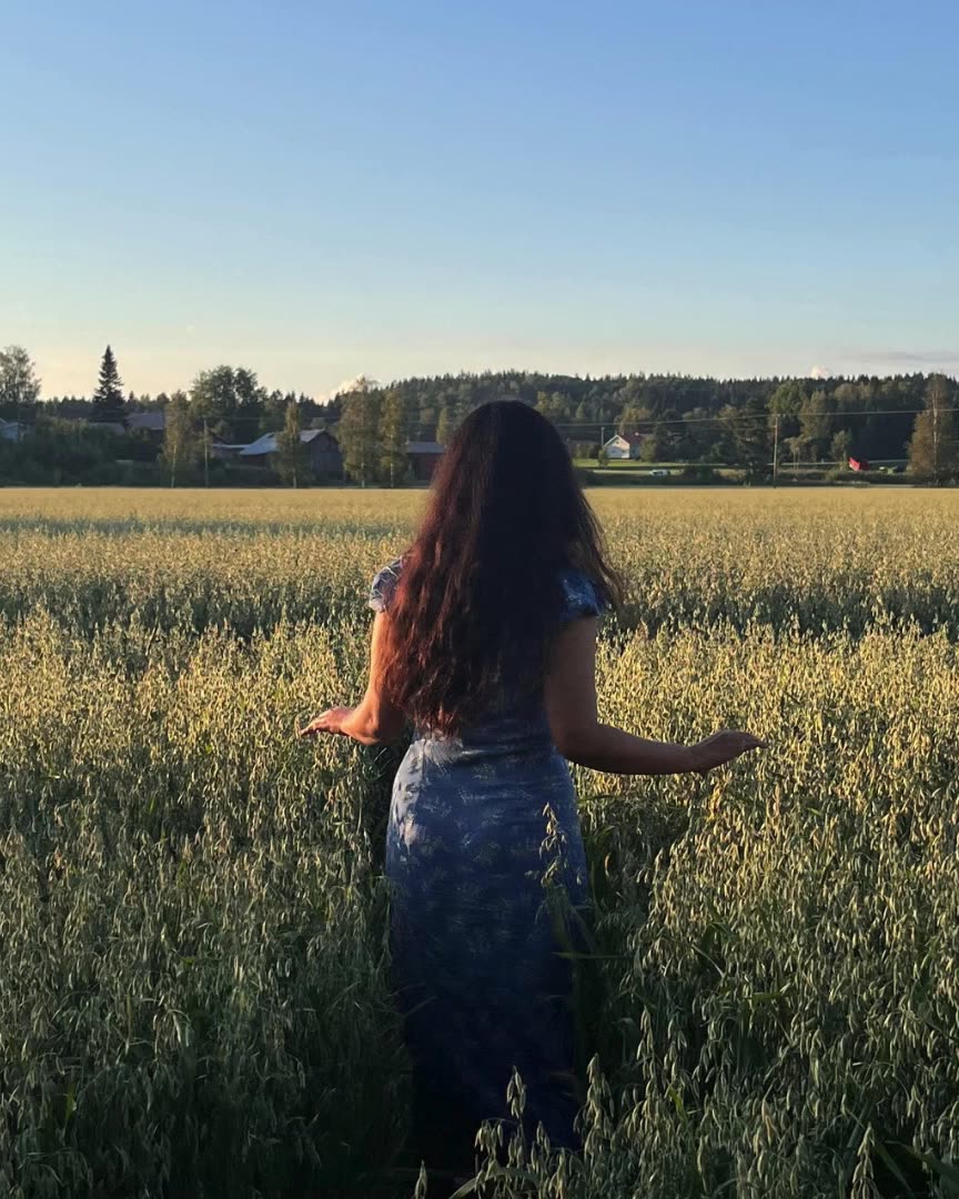 A woman walking into a field of oats at golden hour
