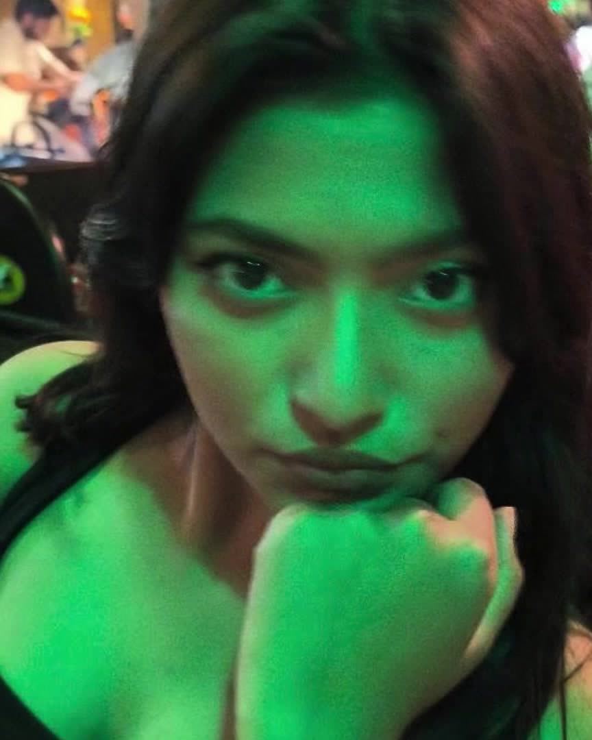 A woman in a bar lit green, chin on her fist